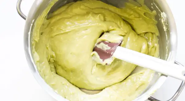 Una spatola mescola una densa crema al pistacchio in una ciotola d'acciaio.