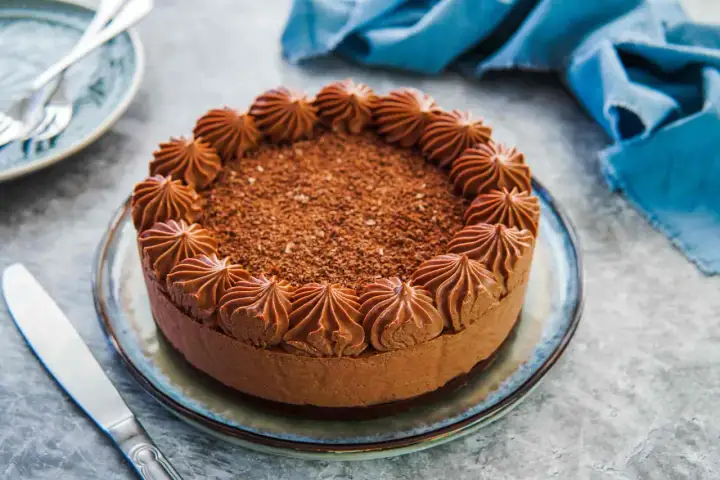 Delizioso cheesecake al cioccolato con decorazioni a ciuffi e scaglie di cioccolato. Un coltello da burro è pronto per essere usato.