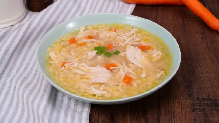 Un confortevole brodo di pollo con pezzi di pollo sfilacciato, carote e un rametto di prezzemolo.